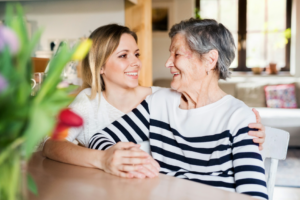 Family caregiver sitting with elderly mother at home, sharing a warm moment together